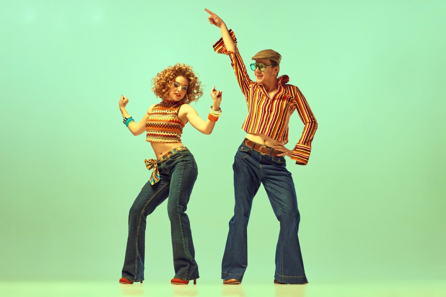 Happy and active dancers. Two excited people, man and woman in retro style clothes dancing disco dance over green background. 1970s, 1980s fashion, music, hippie lifestyle