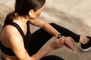 Tired millennial european woman athlete in sportswear checks pulse on fitness tracker in city, outdoor. Result body care, cardio training and fitness, gadget for active workout