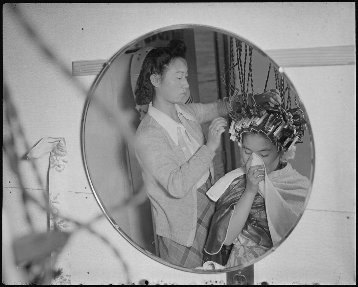 A beauty shop operator working on a client with rollers in her hair.