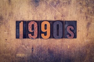 The word "1990s" written in dirty vintage letterpress type on a aged wooden background.