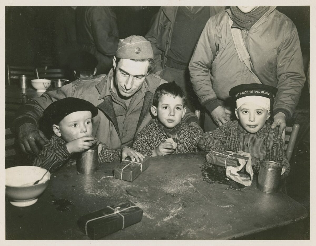 Pfc. Raymond Cyr, St. Albans, Vt., watches his 2 'adopted' children to see that they get enough to eat during Red Cross Christmas party held for about 200 Italian orphans. 24 Dec, 1944.