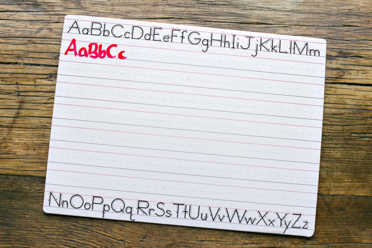 Top view of a white penmanship board with the letters ABC written in red marker by a child