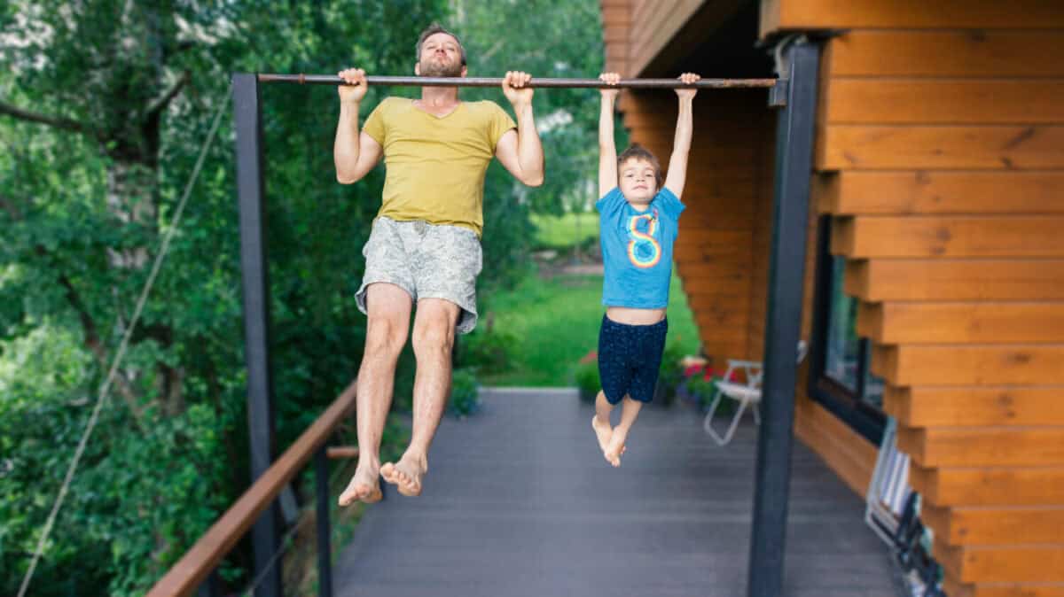 A boy pulls himself up on the bar. The son and father go in for sports. Sports family in training.The father teaches his child to achieve goals. Summer family outdoor sports workouts in the country.