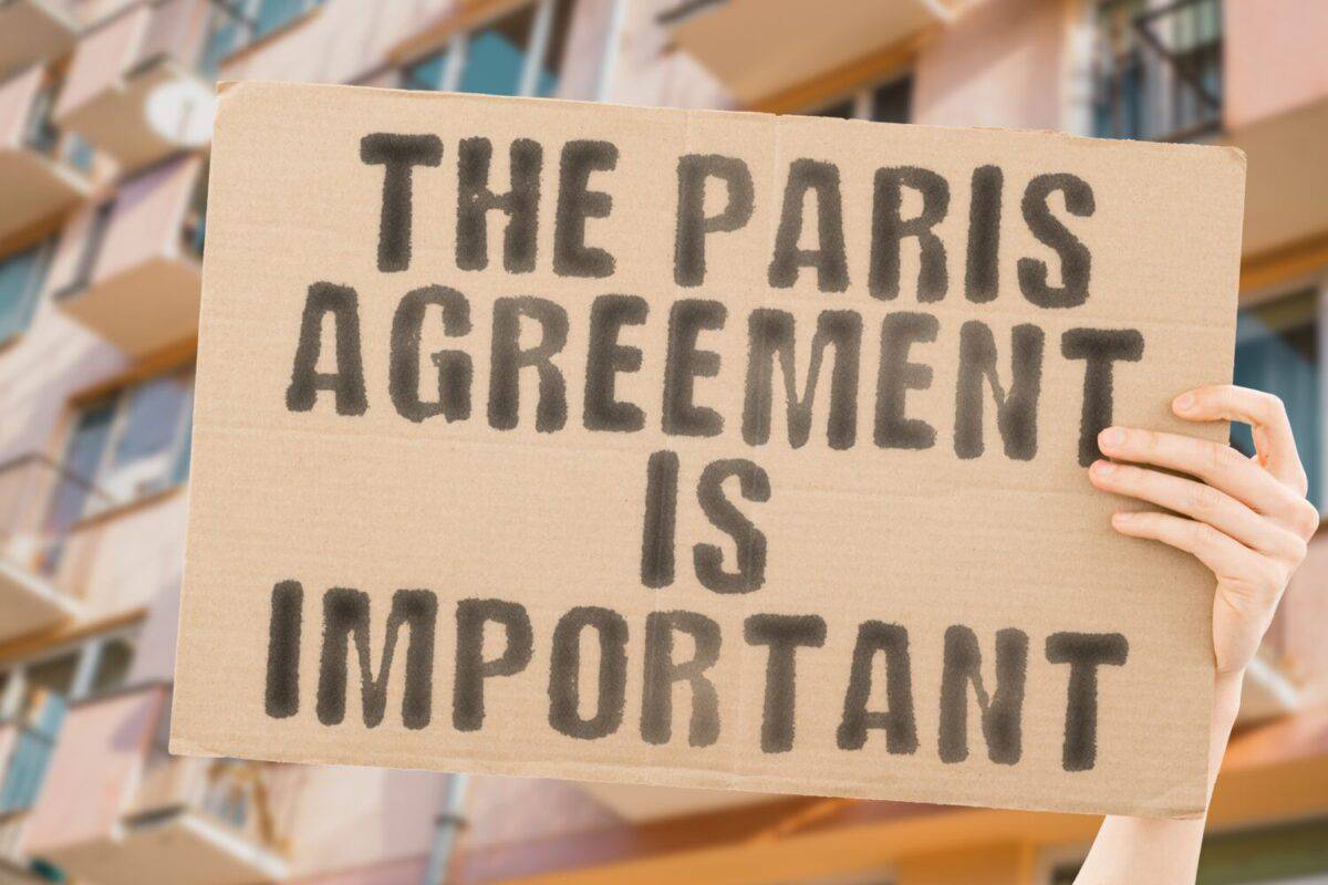 The phrase " The Paris agreement is important " is on a banner in men's hands with blurred background. Resource. Warm. Rights. Rise. Target. Protest. Warming. America. Carbon. Crisis. Power. Global