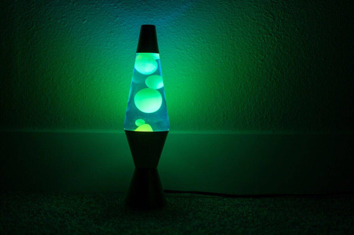 Green lava lamp stands near a white wall in the darkness