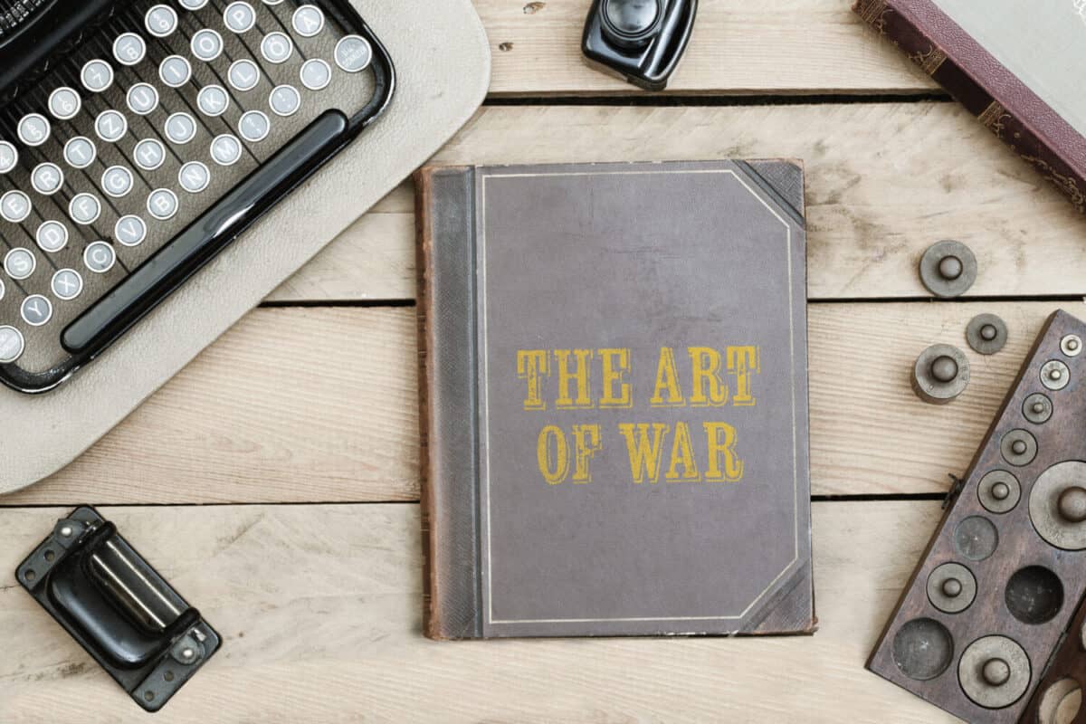 The Art of War text on cover of old book on office desk with vintage type writer machine from 1920s and other obsolete office items.