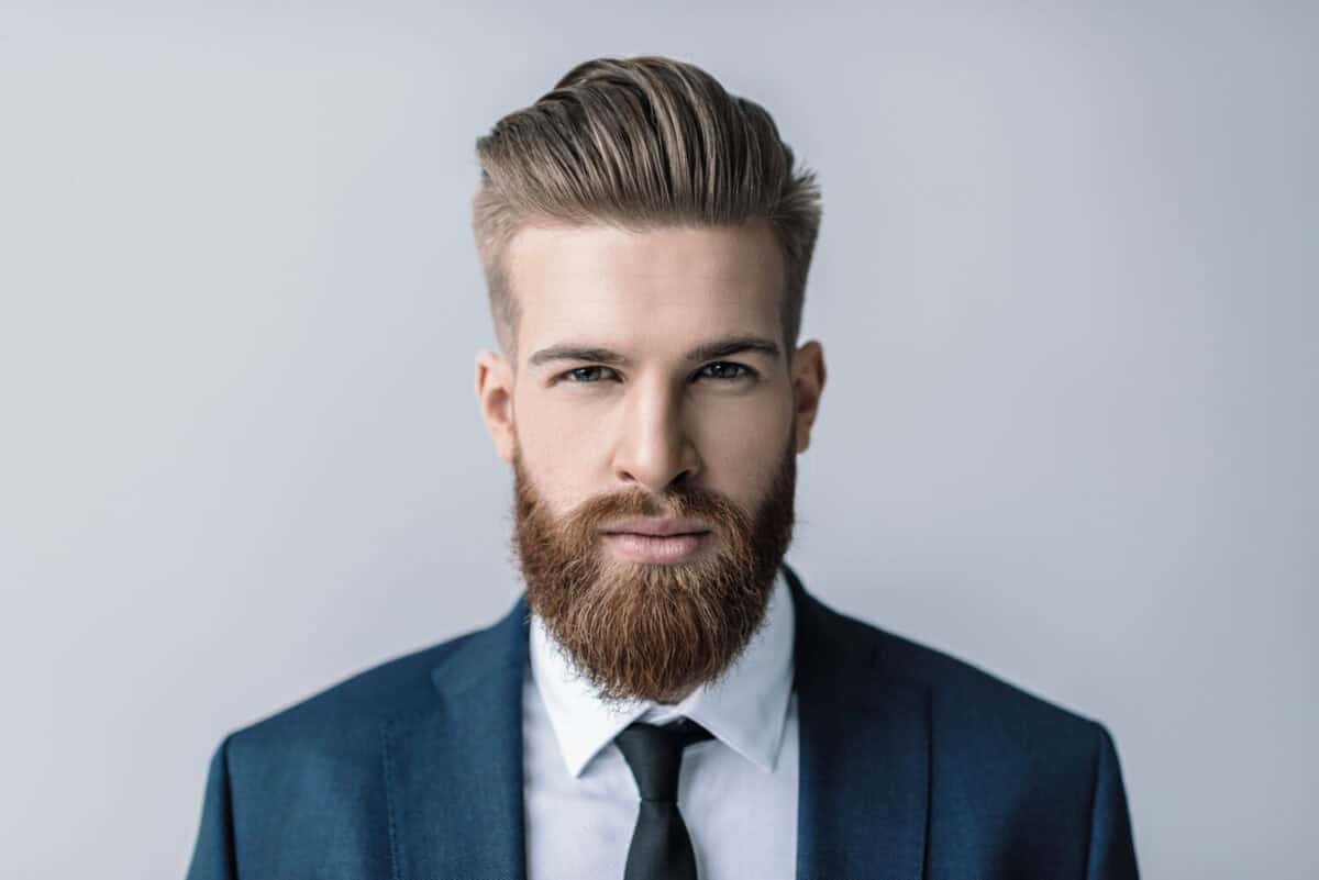 Stylish handsome bearded businessman looking at camera isolated on grey