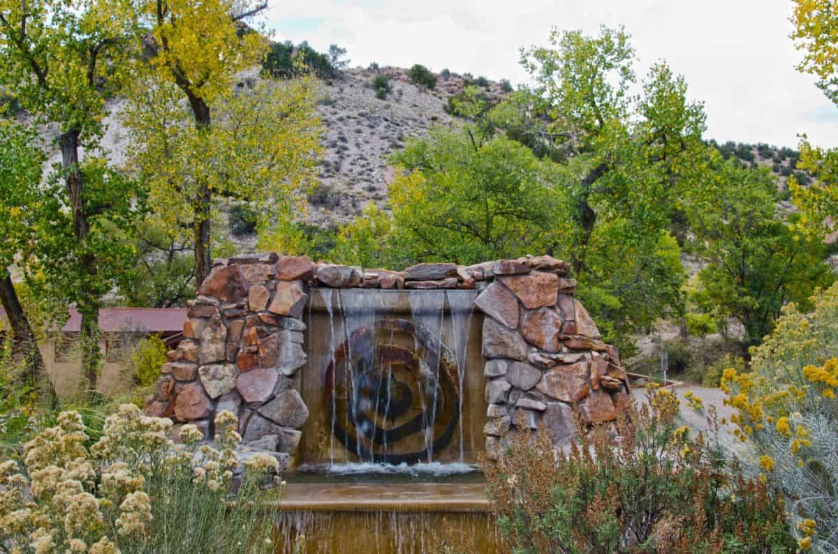 The entrance to Ojo Caliente Hot Springs in New Mexico is marked by a sandstone fountain. The resort stands between rugged hills and the river for which is is named.