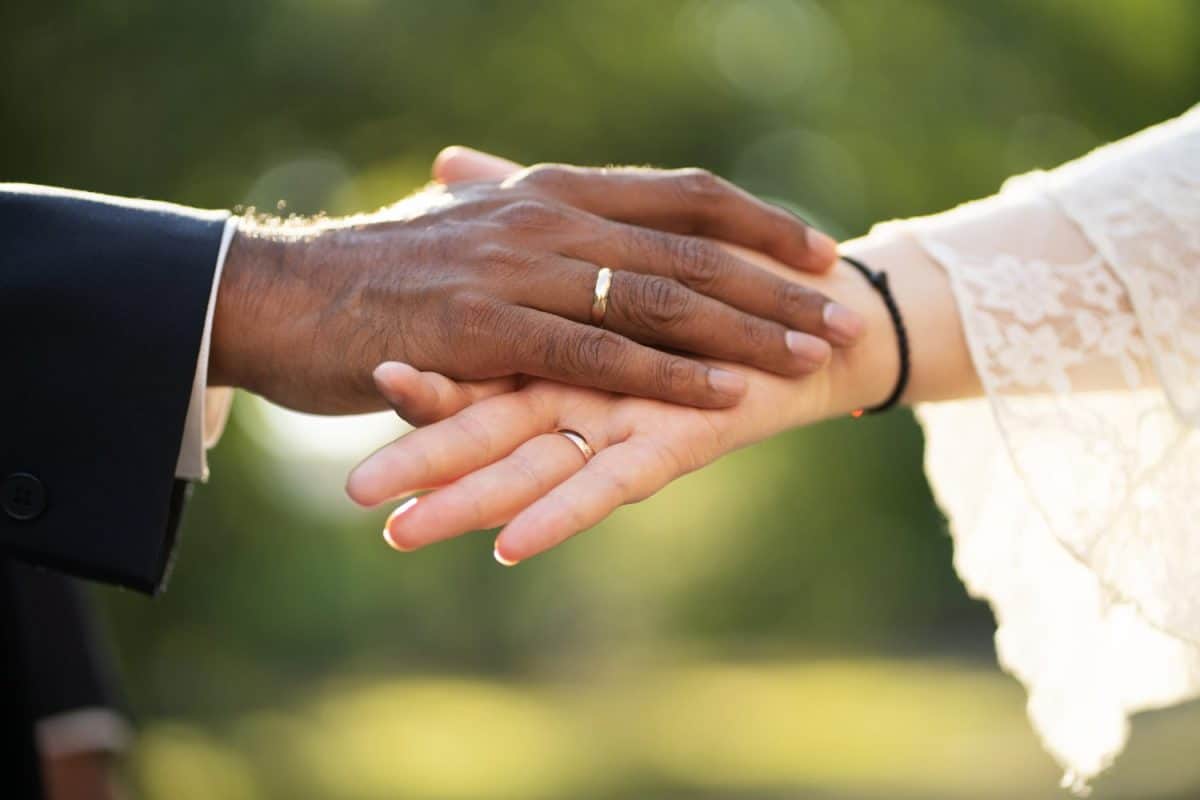 The hands of the bride and groom with the rings close up. A pair of hands of a dark-skinned groom and white bride with rings gently touch each other. The interracial marriage concept.