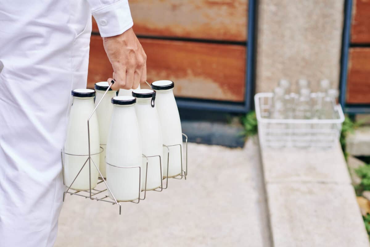Close-up image of delivery man carrying bottles of fresh milk to entrance door