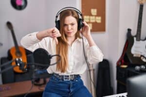 Young caucasian woman recording song at music studio with angry face, negative sign showing dislike with thumbs down, rejection concept