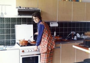 Vintage roll fillm, 1970's woman wearing an orange squared pant and vest cooking dinner on a gas stove.
