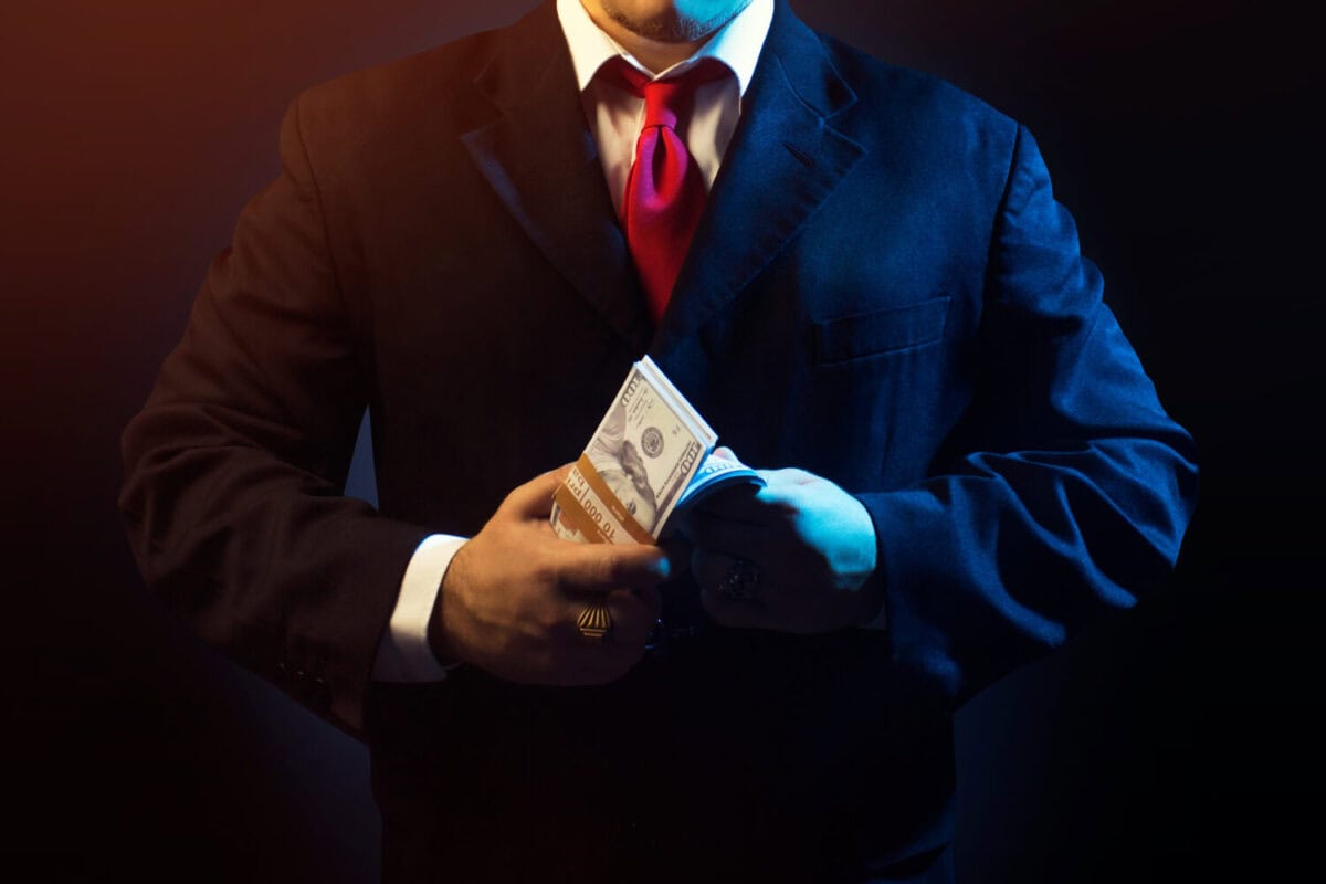 Mafia man in suit counting money on black background.