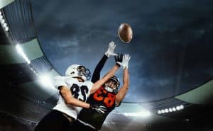Dynamic shot of male sportsmen, professional american football players during game, catching ball. Open air 3D stadium in evening