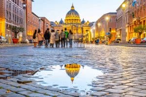 Vatican City by night. Illuminated dome of St Peters Basilica and St Peters Square. Group of tourists on Via della Conciliazione. Rome, Italy.