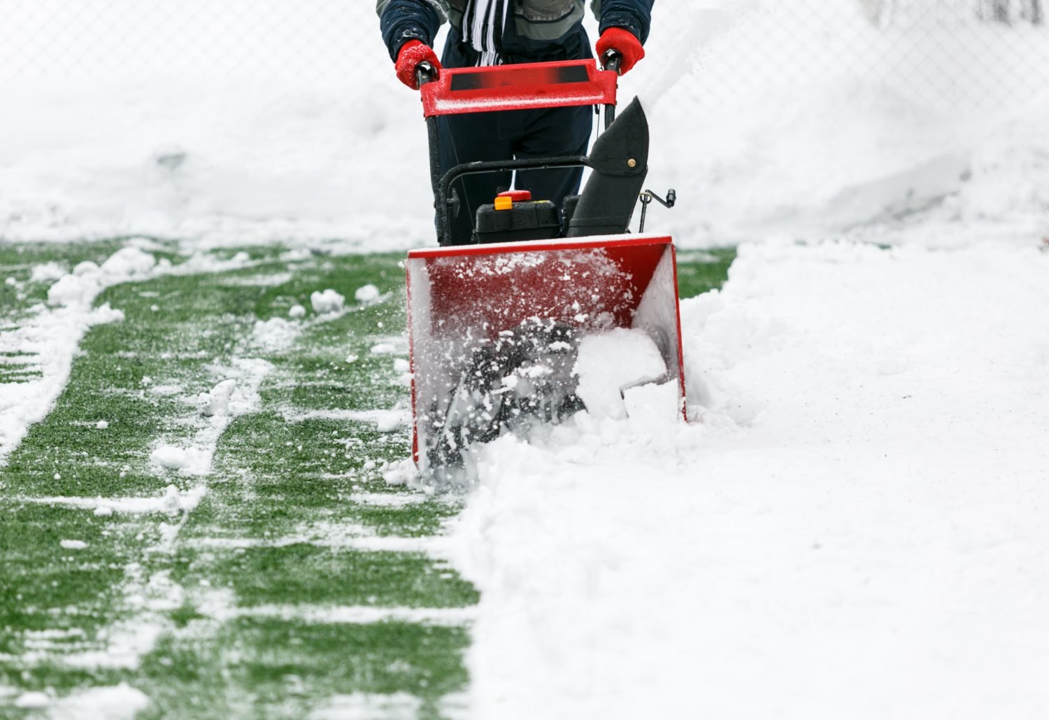 Man using a snow blower to remove large amounts of snow on football field. Man cleans snow with a snow-removing machine on soccer pitch.