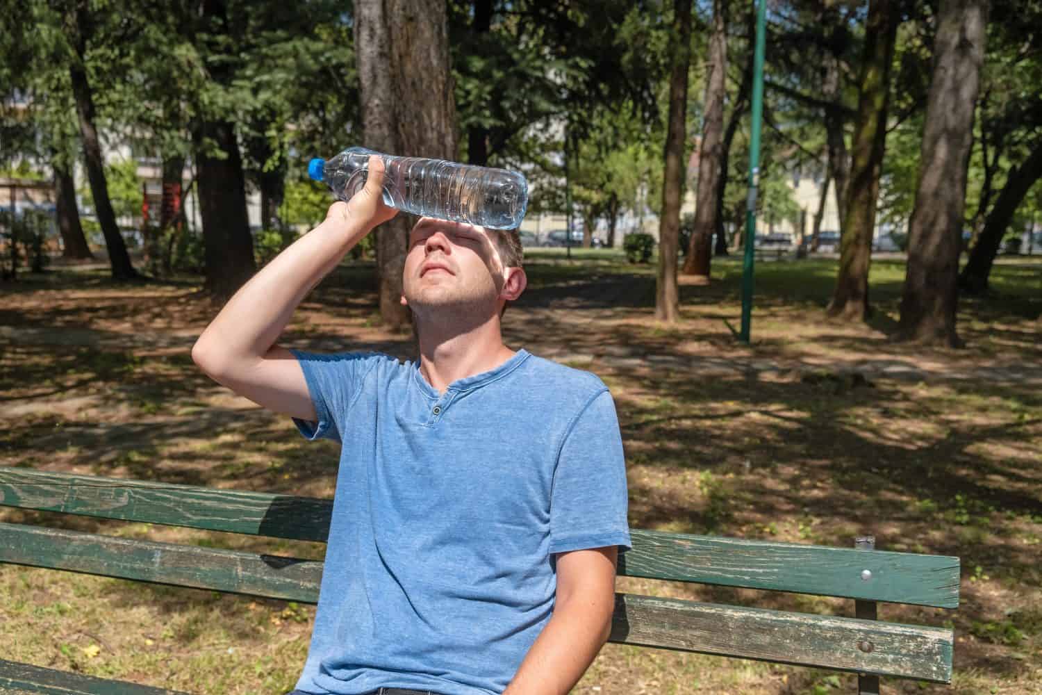 Man suffering from heat wave Charon in South Europe. Caucasian male presses bottle of water to face to cool off suffering from heat sitting outdoors