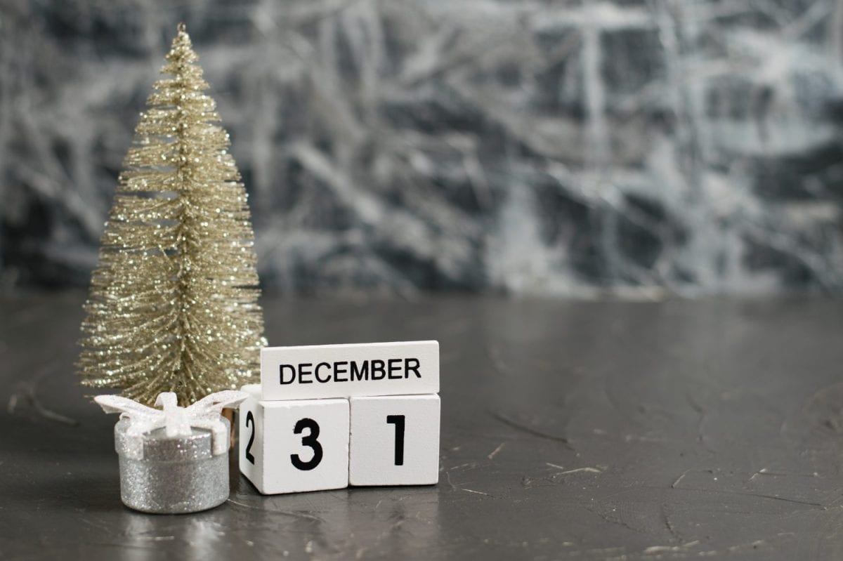 Wooden calendar with December 31 date and beautiful Christmas decoration on dark textured background with copy space.