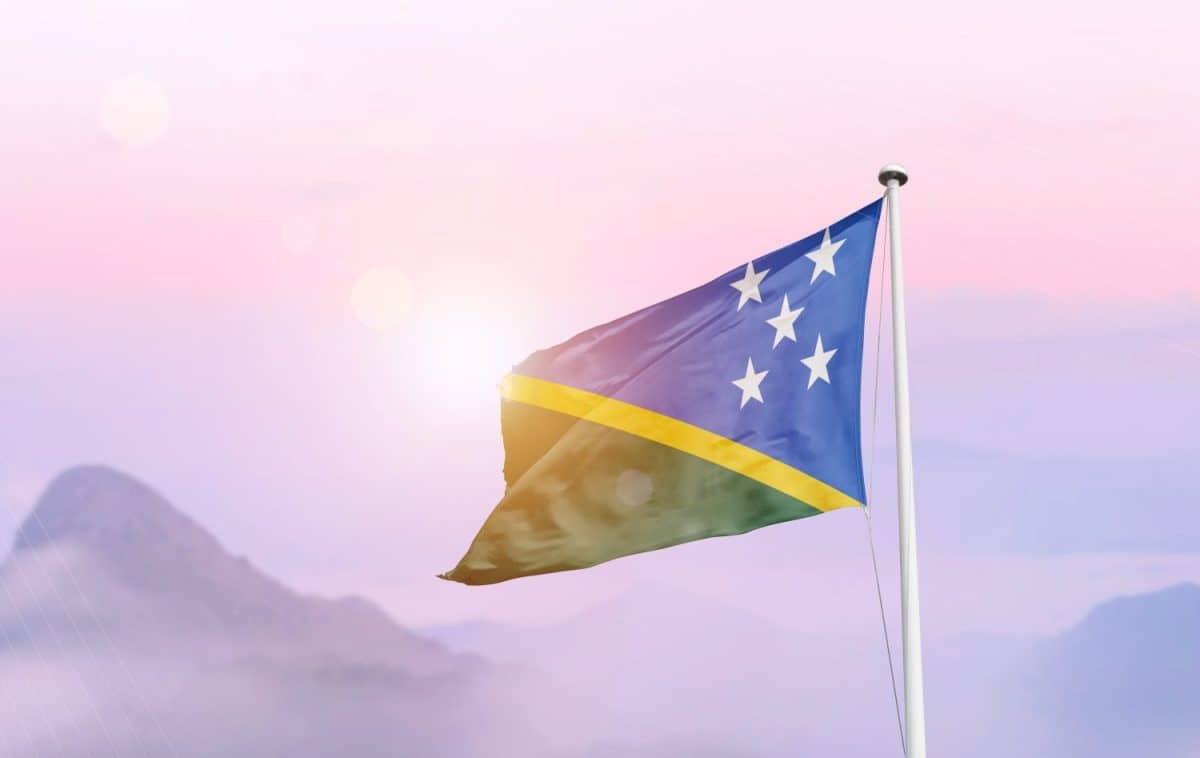 Solomon Islands flag waving on sky pink pastel soft cloud with misty mountain landscape.