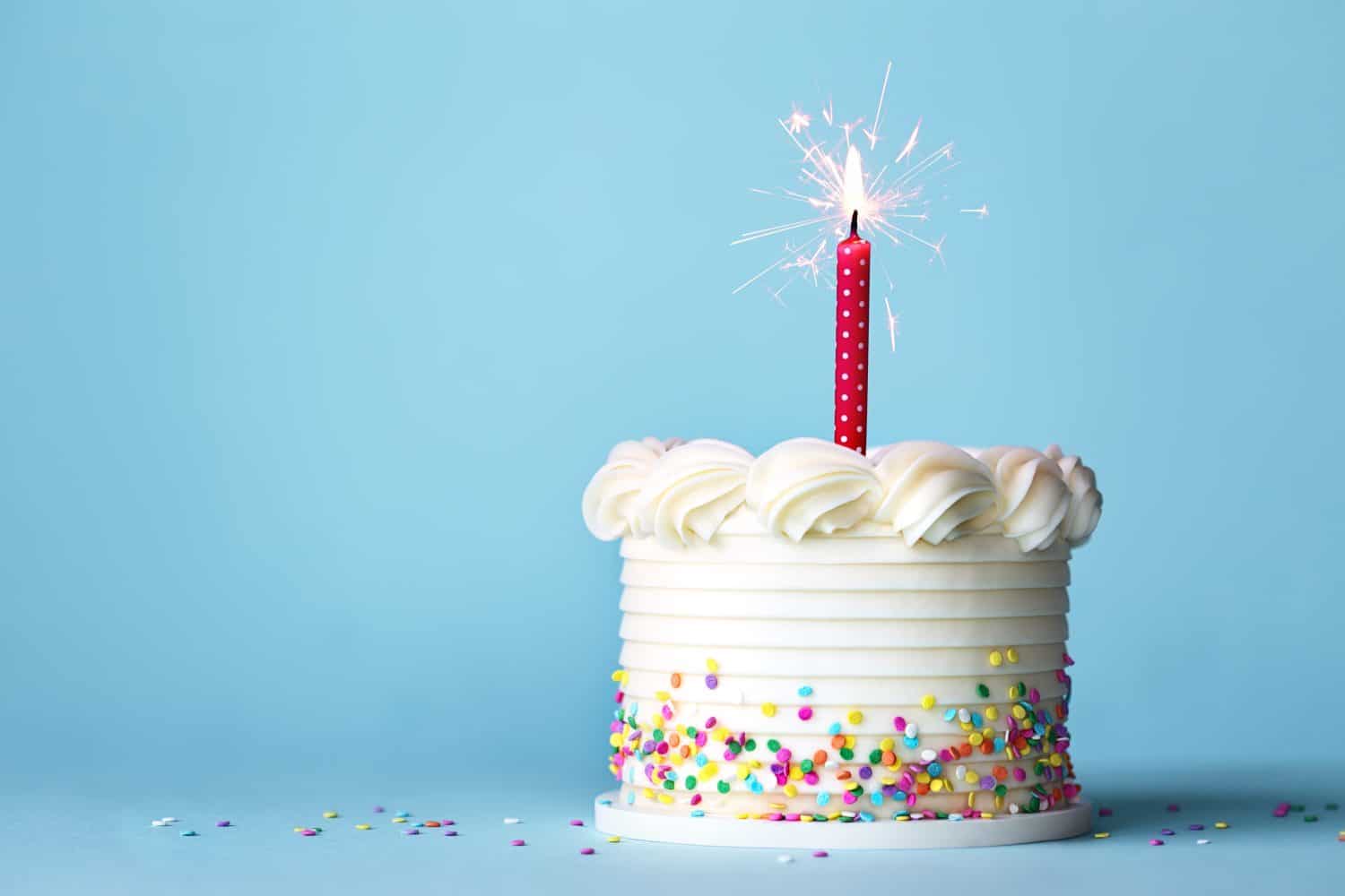 Birthday cake with colorful sprinkles and one red birthday candle against a plain blue background