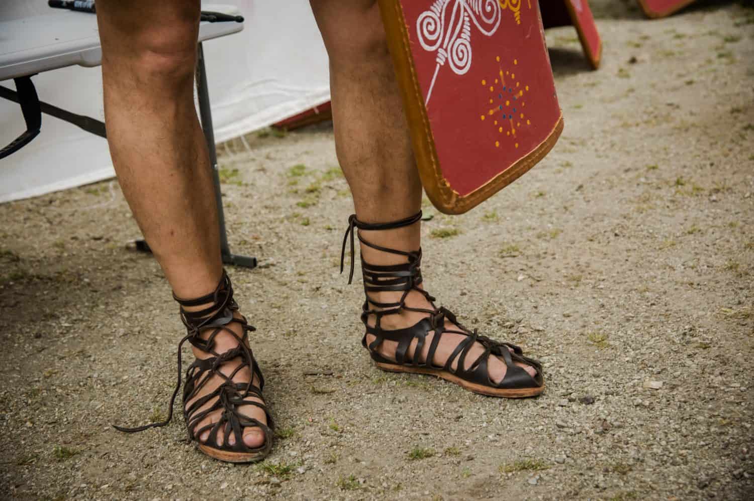 A person donning Roman sandals and holding a Roman shield, representing the ancient warriors of Rome.