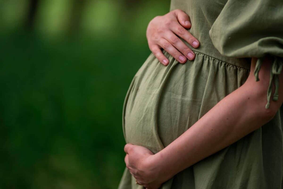 Caucasian Young Pregnant woman Tummy belly summer green dress touching stomach field expecting a baby relaxing outside nature park lake rural Beautiful magic 8 months enjoying life glasses hat