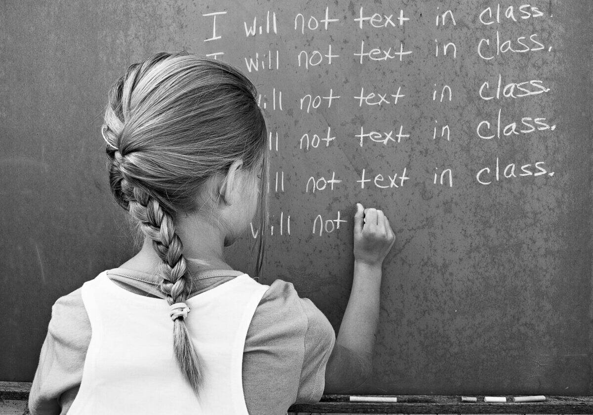 young student writing lines on a school chalkboard