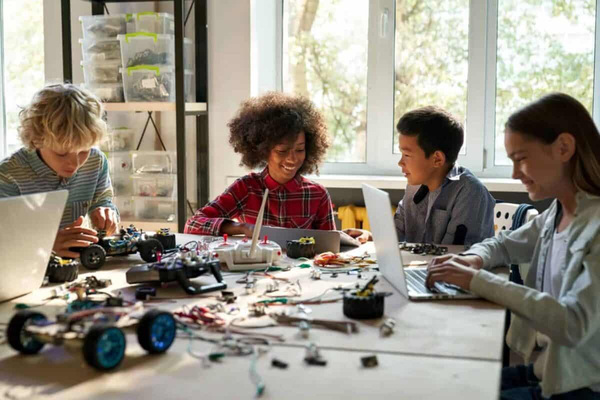 Group of multiethnic schoolkids interacting using gadgets for programming for robotics engineering class. Elementary school science classroom of futuristic technologies. STEM education concept.