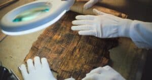 Close up of two archaeologists in gloves carefully opening ancient Egyptian papyrus on table in archaeological lab. Scientists work with cultural heritage of extinct human civilization. Archaeology.