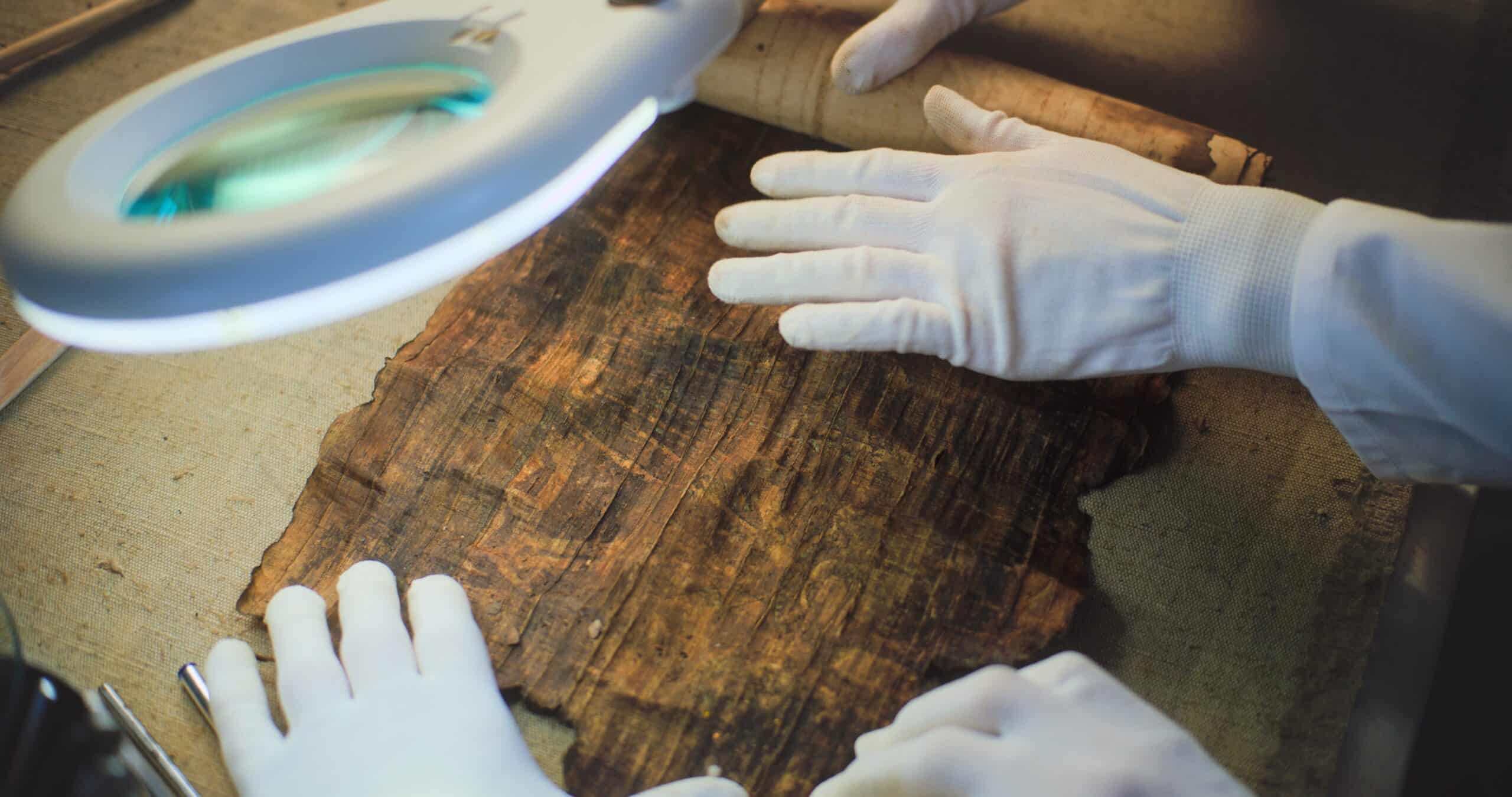 Close up of two archaeologists in gloves carefully opening ancient Egyptian papyrus on table in archaeological lab. Scientists work with cultural heritage of extinct human civilization. Archaeology.