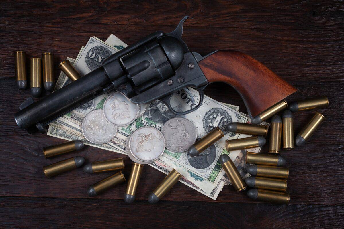 Old west Colt Peacemaker and US banknotes and silver certificates with silver dollar coins and .45 caliber revolver ammunitions background