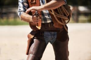 Cowboy, confrontation and aim gun to shoot for standoff or gunfight in duel for wild western culture in Texas. Male gunslinger or outlaw, revolver and tough for defense or conflict with closeup
