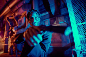 Portrait of a wounded action hero man aiming a gun in the light of the night city.